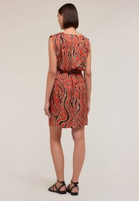 Vestido de patrón rojo y marrón con un corte holgado, mangas cortas y cintura elástica. Presenta elementos de diseño ondulados y una textura suave.