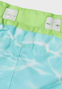 Lichtblauwe zwembroek met een golvend waterpatroon. Heeft een groene elastische tailleband met knoopsluiting en witte stikdetails.