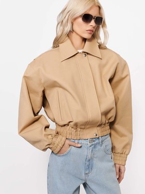 Blondynka w oversize beżowej kurtce z elastycznymi mankietami i dołem, jasnoniebieskich dżinsach z wysokim stanem, okularach przeciwsłonecznych oraz kolczykach w kształcie gwiazdy.