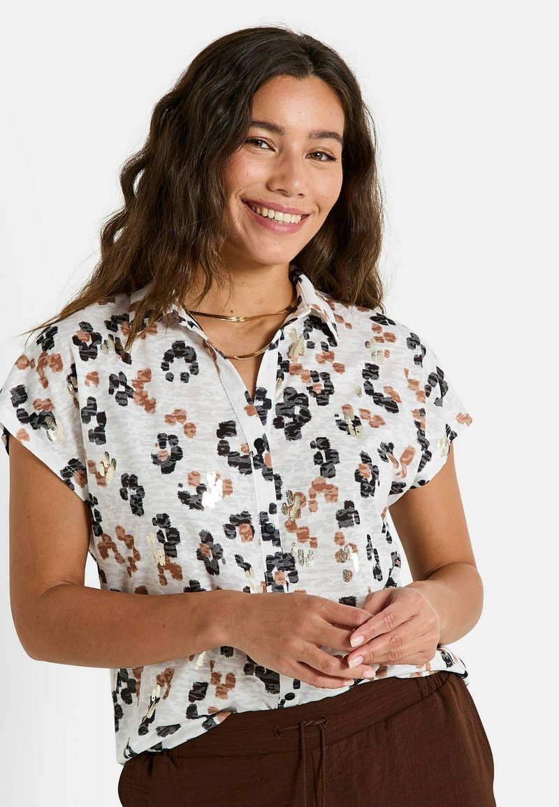 Chemise à manches courtes et à boutons présentant un fond blanc avec un imprimé léopard multicolore dans des tons de marron, noir et accents dorés.