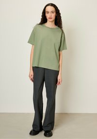 Brīvi pieguļošs olīvzaļš T-krekls ar īsām piedurknēm, kas saskaņots ar pelēkiem šuvējiem biksēm. Sakarā ar melnām platformas kurpēm, apģērbs ir pabeigts. Minimālistiskais dizains.