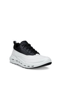 Baskets basses avec tige noire et semelle blanche, présentant des ouvertures de ventilation et des lacets noirs, orientées vers la droite sur fond blanc.