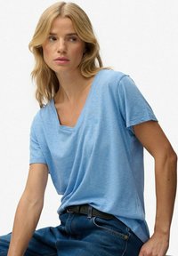 Lyseblå kortærmet T-shirt i et blødt, struktureret stof med V-hals og en lille logo-detalje på brystet. Sammen med mørke jeans.