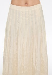 Gonna maxi plissettata in beige chiaro, realizzata in un tessuto trasparente e testurizzato. Presenta righe verticali e una vita elasticizzata.