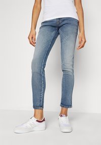 Jasnoniebieskie skinny jeans wykonane z denimu, z średnim stanem i lekko przetartym wykończeniem. W połączeniu z białymi trampkami.