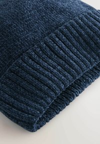 Tumed sinise värvi kudumine beanie, millel on tekstureeritud soonikkoonus ja sile keha, valmistatud pehmest villasegust soojuse ja mugavuse tagamiseks.