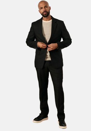 Blazer negro a medida sobre una camiseta de cuello redondo a rayas, combinado con pantalones negros y zapatillas negras con suela blanca.