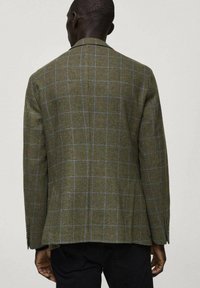 Blazer a scacchi in verde oliva con accenti blu. Vestibilità tailored, a lembi a punta e tessuto testurizzato. Presenta tre bottoni sulle maniche.