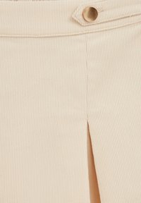 Tissu en velours côtelé beige avec des côtes verticales, comportant un unique bouton en métal à la taille et un détail fendu sur la couture latérale.