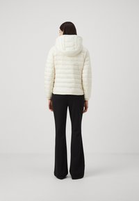 Lätt krämfärgad pufferjacka med huva och horisontellt quiltat mönster, i kombination med figurnära svarta utsvängda byxor. Slät textur, minimalistisk design.