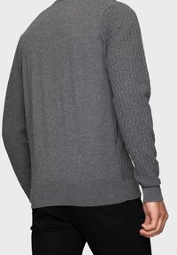 Suéter gris de cuello redondo con un patrón texturizado en las mangas y cuerpo liso, con puños y dobladillo acanalados.