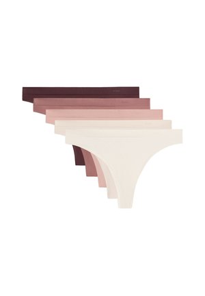 Femme portant un sous-vêtement style bikini blanc uni sans couture, avec une texture lisse et une ceinture élastique sur fond blanc.