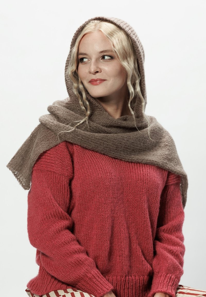 Sweter dzianinowy w głębokim czerwonym kolorze o luźnym kroju i ściągaczu, połączony z miękkim beżowym szalem o teksturowanym wykończeniu. Wzory na dolnej części odzieży.