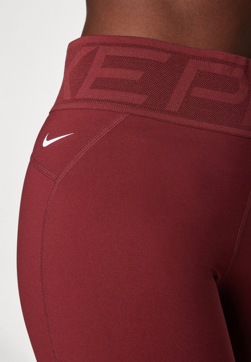 Leggings bordeaux con una cintura ampia caratterizzata da un motivo testurizzato e logo Nike bianco. Tessuto morbido e dettagli di cucitura a contrasto.