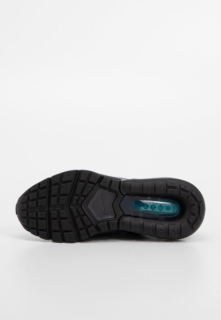 Suela de zapatilla Nike, goma negra con un patrón de tracción multidireccional. Cápsula de amortiguación en color teal visible, con surcos hexagonales y rectangulares en toda la superficie.