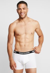 Weiße Baumwoll-Boxershorts mit einem schwarzen elastischen Bund, der mit "URBAN CLASSICS" beschriftet ist, taillierte Passform, glatte Textur, Oberschenkel-lange.