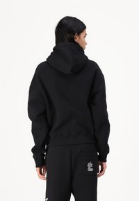 Moleton preto com um capuz espaçoso, punhos e bainha canelados. Apresenta um bolso lateral com um design decorativo. O material parece suave e texturizado.