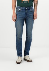 Jean skinny en denim, avec un design classique à cinq poches et un léger délavage, associés à des baskets claires.