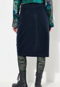 Námořnická kordová midi sukně s rozparkem vzadu, zkombinovaná se zelenými krajkovými punčochami a černými koženými šněrovacími botami. Na pase je vidět vzorovaná blůza.