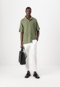 Camicetta corta a maniche verdi con texture, pantaloni bianchi su misura, mocassini neri in pelle e una borsa a tracolla nera in pelle.