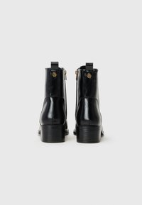 Black leather ankle boots with a smooth texture, zip closure, and gold accents; features a stacked heel and pull tab at the back.