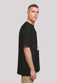 Sort bomulds t-shirt med en løstsiddende pasform, korte ærmer og et grafisk print på forsiden, vist på en model fra siden.