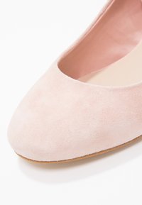 Růžové semišové baleríny s kulatou špičkou a hladkým vnitřkem. Svršek má měkkou texturu a podešev je lehká a plochá.