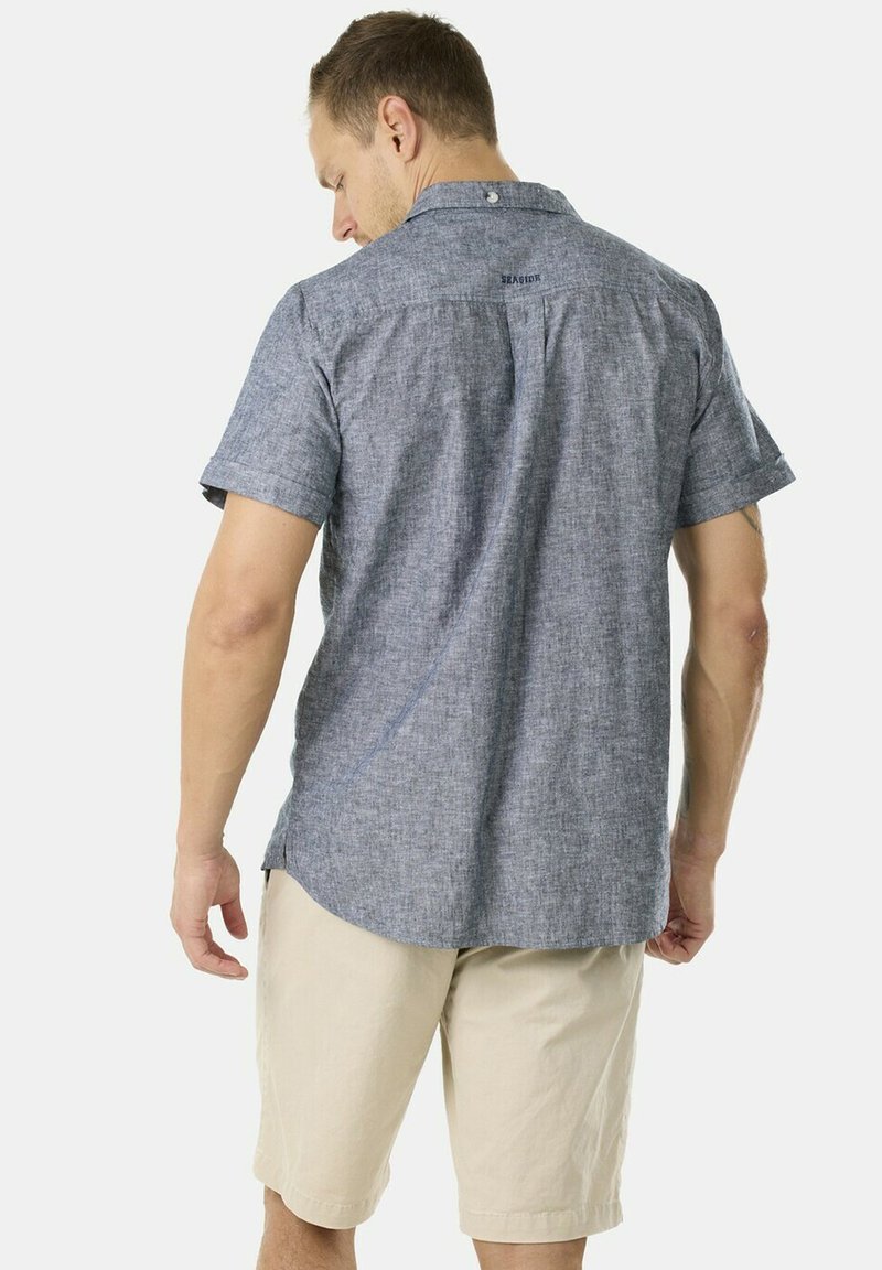 Kortärmad blå, texturerad skjorta med knapp-ner krage och logodetalj på ryggen, i kombination med beiga shorts. Avslappnad och lätt.