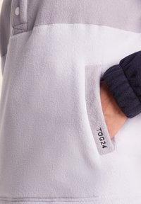 Fleece pullover in light gray and white with a navy cuff. Features a chest pocket and the label "TOG24" stitched on the pocket seam.