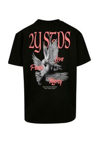 Melna kokvilnas T-krekls ar grafiku, uz kuras attēloti divi balti baloži ar izplestām spārniem, ko papildina rozā teksti "Miers", "Mīlestība" un "Žēlsirdība."