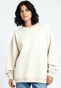 Sweatshirt oversize crema realizzato in morbido tessuto, con polsini e orlo a coste, dalla vestibilità rilassata e con dettagli di cucitura minimi.