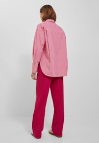 Pink and white striped oversized shirt with long sleeves, back pleat, and rounded hem, paired with bright pink wide-leg pants.
