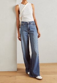 Top sin mangas de color gris claro combinado con jeans de pierna ancha azul, que cuentan con bolsillos estándar y un diseño clásico de cinco bolsillos, complementado con zapatillas blancas.