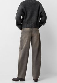 Grå stickad tröja med ribbad kant, tillsammans med löst sittande, ljusgrå tapered jeans med bakfickor, och svarta klumpklackar.