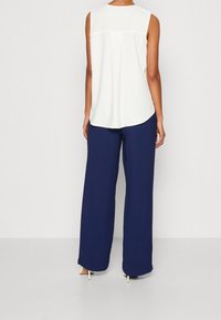 Haut blanc sans manches avec un ourlet arrondi, associé à un pantalon large bleu marine. Tissu simple et texturé, sans motifs ni accents visibles.