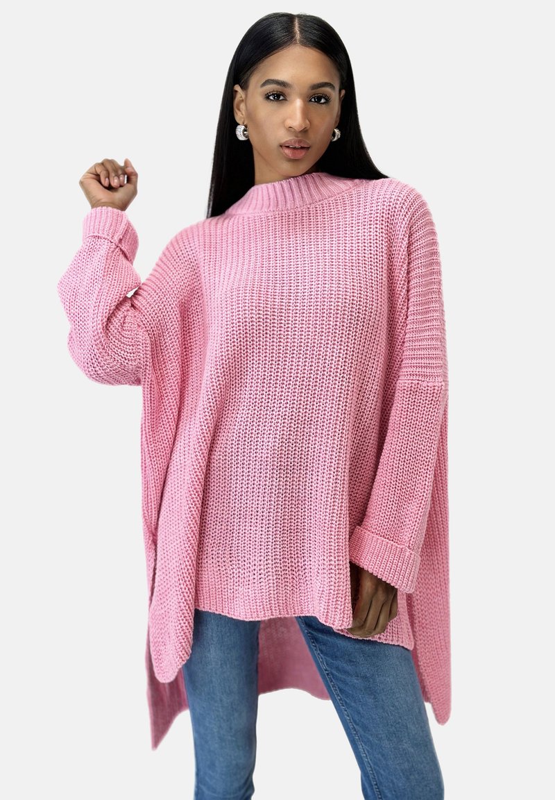 Rosa stickad oversized tröja med hög krage, sänkta axlar och ribbade ärmslut, ihopparad med blå smala jeans.