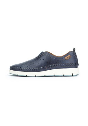 Zapatos de cuero azul marino tipo mocasín con diseño perforado, detalles en beige y suela de goma blanca. Presentan costuras decorativas a lo largo de los bordes.