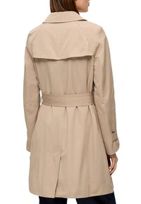 Beige trenchcoat met een ceintuur in de taille, dubbele knopen en een brede kraag. Bevat een rugventilatie voor meer bewegingsvrijheid.
