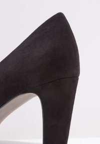 Chaussure à talon haut en daim noir avec un bout pointu et un talon épais. La texture est douce avec une doublure intérieure lisse. Design simple et élégant.