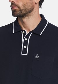Marineblauwe poloshirt van katoen, met een witte kraagafwerking, drie knopen en een klein pinguïnlogo op de borstzak.