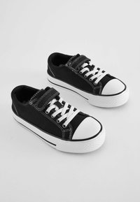 Sorte kanvas sneakers med hvide gummisåler, markante hvide snørebånd og en Velcro-rem. Har hvid syning og en rund tå.