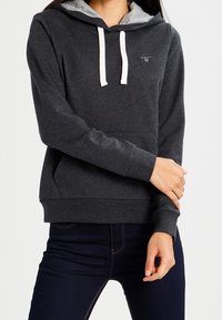 Donkergrijze hoodie met een lichtgrijze voering in de capuchon, trekkoorden en een voorste kangoeroezak. Zachte stof met een losse pasvorm.