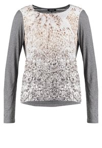 Långärmad topp med en grå jersey-kropp och mönstrad lättviktsfabrik framtill som har nyanser av beige och vit blommönster.
