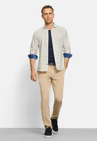 Herrenoutfit mit einem hell gemusterten Hemd mit blauen Manschetten, einem marineblauen T-Shirt, cremefarbenen Hosen und dunklen Sneakers. Lässiges, zeitgemäßes Design.