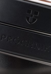 Czarny skórzany pojemnik na przechowywanie z wytłoczonym napisem "PRÓCHNIK" i logo, o gładkiej fakturze i eleganckim designie.