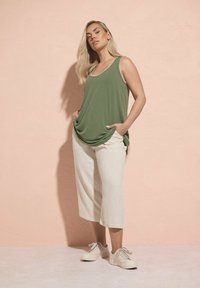 Olivgrön ribbad linne med rundad halsringning, parat med ljusbeiga vida linbyxor och ljusa sneakers.