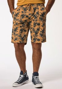 Korte tan shorts met zwart tropisch bladpatroon, trekkoord in de taille, zijzakken en een relaxed fit, gecombineerd met marineblauwe hoge sneakers.
