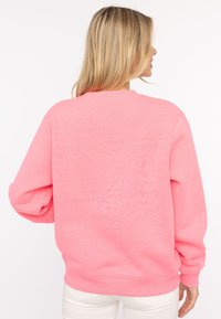 Rosa Sweatshirt mit Rundhalsausschnitt, langen Ärmeln und lockerer Passform. Weicher Stoff mit gerippten Bündchen und Saum. Schlichte Rückseite.