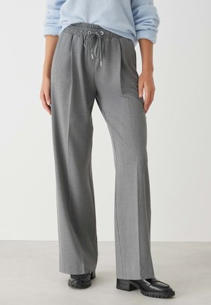 Graue, plissierte Hose mit elastischem Bund und Kordelzug. Schmal zulaufendes Design, strukturierten Stoff, getragen mit schwarzen, klobigen Loafern.