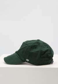 Casquette en coton vert avec une visière courbée, présentant un patch logo rond et un détail brodé "24/7" sur le côté. Le design est structuré et décontracté.